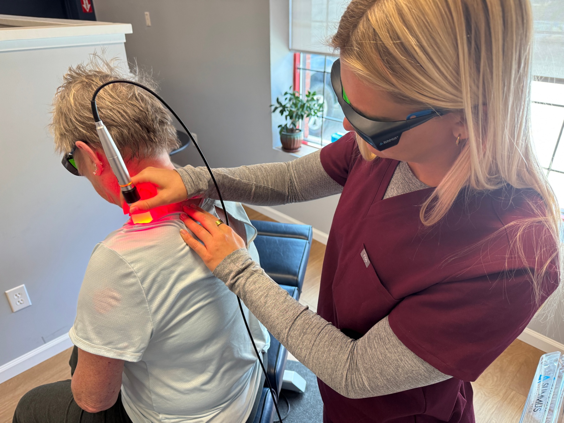 Assistant performing laser therapy on a patient's neck